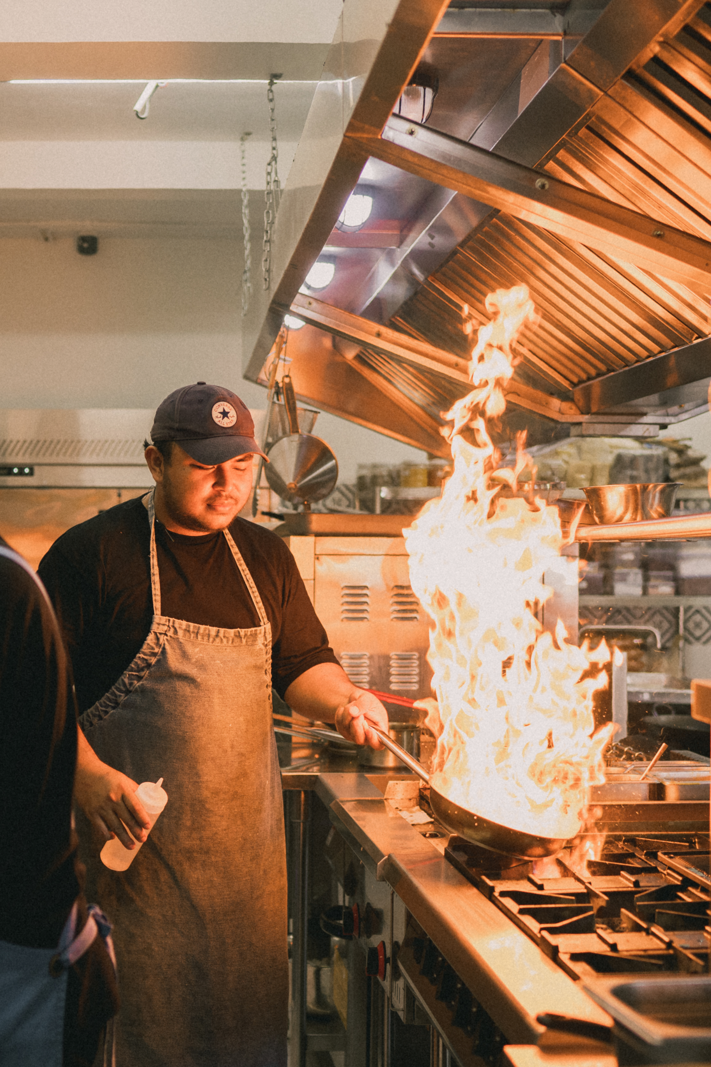 A man in an apron cooking in a kitchen with flames.
